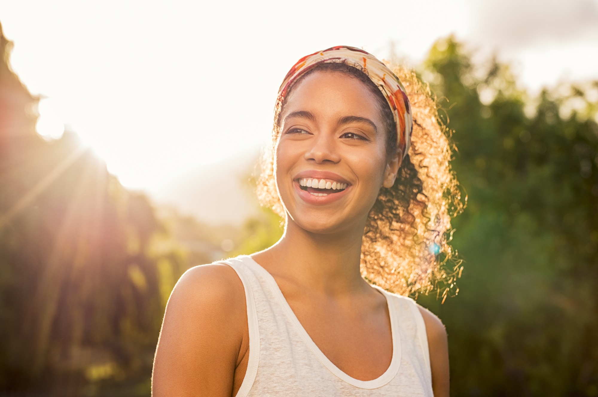 Portrait of beautiful woman smiling and looking away at park during sunset